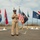 C3F conducts Chief pinning ceremony A U.S. Navy enlisted service member in khaki service uniform stands at a microphone addressing an audience at an outdoor military ceremony. The setting appears to be a coastal overlook or memorial area with multiple state flags, the U.S. national flag, and a POW/MIA flag displayed on poles behind the speaker. The ocean is visible in the background under a partly cloudy sky.