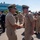 C3F conducts Chief pinning ceremony Two U.S. Navy senior enlisted personnel are shaking hands in the foreground during what appears to be a formal military ceremony or change of command event. Both are wearing khaki service uniforms with combination covers, and the individual on the right displays multiple service ribbons. A formation of Navy personnel in matching uniforms stands in the background alongside civilian spectators.