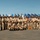 C3F conducts Chief pinning ceremony A large group of U.S. Navy personnel in tan/khaki service uniforms pose for a formal group photograph outdoors. They are arranged in multiple rows with a display of numerous military flags and pennants behind them. One individual near the center is wearing a colorful lei, suggesting a ceremonial or special occasion, possibly in Hawaii.