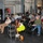 xTechAutonomy Phase II Live Demonstrations A group of approximately 15-20 people are gathered in what appears to be an industrial or garage-style venue for a presentation or informational event. A banner for 'Mesodyne' is prominently displayed at the front, suggesting this is a company demonstration or pitch event. Attendees are seated in folding chairs while some stand along the periphery, with several taking notes.