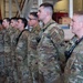 A formation of U.S. Air Force personnel standing at attention inside what appears to be a fire station hangar. The individuals are wearing Operational Camouflage Pattern (OCP) uniforms with visible 'U.S. AIR FORCE' and 'FIRE' patches, along with radio communication devices. The group appears to be participating in a formal military ceremony or inspection.