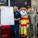 Five individuals pose for a group photo at Eielson AFB, Alaska, during a Fire Prevention Week Proclamation ceremony for the 354th Fighter Wing. The group includes military personnel in Army Combat Uniforms, a civilian firefighter, a fire safety mascot character named 'Sparky' the Dalmatian, and a civilian official. One person holds a large framed proclamation document titled '354th Fighter Wing – Fire Prevention Week Proclamation, Eielson AFB, Alaska.'