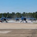 A formation of Blue Angels F/A-18 Super Hornet jets taxi in close formation on an airfield runway. The aircraft are painted in the distinctive blue and yellow color scheme of the U.S. Navy Blue Angels flight demonstration squadron. Heat shimmer and jet exhaust are visible beneath the aircraft as they move along the tarmac.