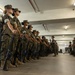 A formation of female military personnel, appearing to be U.S. Marines based on their MARPAT woodland camouflage uniforms and campaign covers, stand at attention in an indoor facility. They are holding M16/M4-style rifles at their sides in a disciplined formation. The setting appears to be a barracks or training facility, consistent with a military inspection or drill exercise.