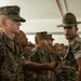 A U.S. Marine Corps drill instructor wearing the distinctive campaign cover (Smokey Bear hat) is inspecting or addressing a formation of recruits in Marine Corps Combat Utility Uniforms (MCCUU). The drill instructor appears to be speaking directly to or inspecting one of the recruits in the front row. The setting appears to be an indoor training facility or receiving bay.
