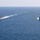 Pre-Commissioning Unit Ted Stevens, USS Daniel Inouye sail together Two U.S. Navy warships are sailing in formation across open blue ocean waters. Both vessels appear to be Arleigh Burke-class guided-missile destroyers, identifiable by their gray hulls, superstructure configuration, and American flags. The ships are traveling on parallel courses with visible white wake trails behind them.