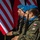 Oleszno cultural center dedicated to Staff Sgt. Michael Ollis, honoring U.S.-Poland bond Three military personnel wearing blue berets and camouflage uniforms stand at attention in a formal ceremony. They are carrying rifles and wearing patches identifying them as Polish military, with blue scarves indicating a UN peacekeeping affiliation. Multiple flags, including the United States flag and what appears to be the Polish flag, are visible in the background.