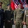 Oleszno cultural center dedicated to Staff Sgt. Michael Ollis, honoring U.S.-Poland bond Four individuals in military uniforms pose together at what appears to be a joint US-Polish military ceremony or event. Two appear to be senior officers (one US Army, one Polish Army), and two appear to be younger cadets or junior personnel wearing blue berets. American and Polish flags are prominently displayed in the background.