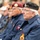 Attendees at the LT John S Thompson Bridge Ceremony, Operation Market Garden Commemorations 2026 The image shows elderly veterans seated at what appears to be a commemorative or remembrance ceremony. Two men in the foreground wear dark blue Legion uniforms with Canadian Royal Canadian Legion badges and berets — one maroon/burgundy and one black. The setting appears to be an outdoor public event with a crowd visible in the blurred background.