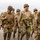 WW2 Reenactors Marching at the LT John S Thompson Bridge Ceremony, Operation Market Garden Commemorations 2026 A group of individuals dressed in WWII-era U.S. Army uniforms are marching along a rural road, likely participating in a historical reenactment or commemorative event. They are wearing M1 helmets, olive drab uniforms, and carrying period-accurate equipment including weapons, ammunition pouches, and field gear. American flag patches and unit insignia are visible on their uniforms.