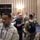 Space Force Connection Time at AFA 2026 A group of military personnel gathered in what appears to be a hotel ballroom or conference facility, suggesting a formal military symposium or conference event. The majority are wearing camouflage uniforms (OCP/MultiCam pattern), while one individual in the center is wearing a dark blue service dress uniform with senior enlisted rank insignia. Attendees are engaged in informal networking conversations throughout the room.