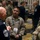 Space Force Connection Time at AFA 2026 A military conference or symposium setting where uniformed personnel are engaged in conversation. The foreground shows three individuals in discussion, including a senior enlisted member in a dark service uniform and two personnel in camouflage uniforms. The background shows a crowded ballroom-style venue with numerous additional military members.