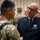 Space Force Connection Time at AFA 2026 Two military personnel are engaged in a face-to-face conversation at what appears to be a formal military gathering or event. The individual on the right is wearing a dark blue Air Force-style service uniform with a name tag reading 'John "BJ" Bentivegna' and displays a Chief Master Sergeant rank insignia. In the background, multiple uniformed personnel in camouflage uniforms are visible, suggesting a multi-branch military event.