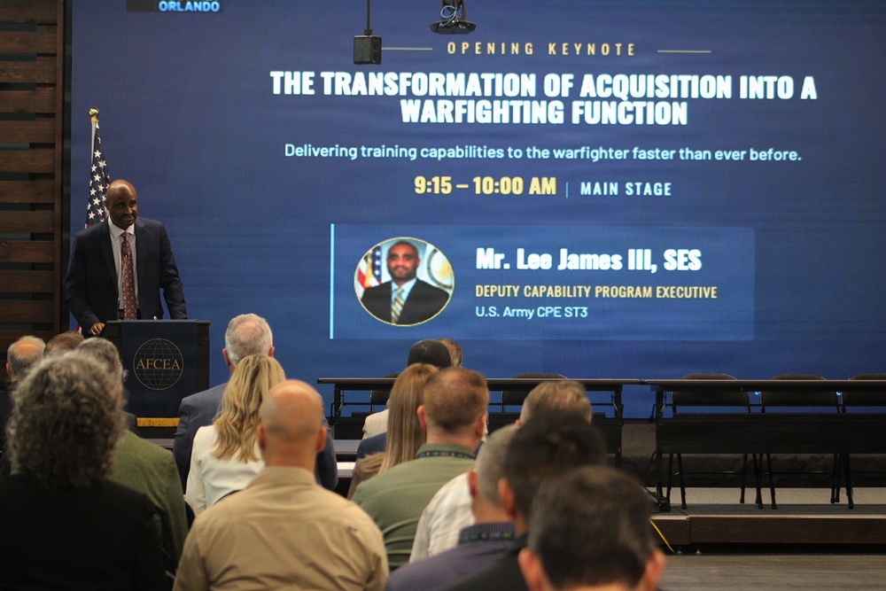 An opening keynote presentation at an AFCEA conference in Orlando, titled 'The Transformation of Acquisition into a Warfighting Function.' A speaker stands at an AFCEA-branded podium addressing a seated audience, with a large presentation screen displaying session details. The featured speaker is identified as Mr. Lee James III, SES, Deputy Capability Program Executive, U.S. Army CPE ST3.