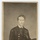 A carte-de-visite (CDV) portrait photograph of a young man identified by handwritten inscription as 'Spencer Kellogg Brown.' He is wearing a dark military or naval uniform with brass buttons and holds a kepi-style cap. The photograph was taken by the Baker studio in Utica, New York, likely during the American Civil War era (1860s).
