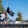 Three individuals are running on an outdoor track while carrying a POW/MIA flag, which is black with the recognizable silhouette emblem and the text 'NOT FORGOTTEN.' The scene appears to be a memorial or commemorative run, likely on a military installation, with a snow-capped mountain visible in the background. The setting suggests the Pacific Northwest region of the United States, possibly near Joint Base Lewis-McChord given the visible mountain resembling Mount Rainier.