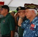 A group of veterans are saluting during what appears to be a military or patriotic ceremony held under a white tent in Hawaii. The foreground figure is identified as Lynn B. Mariano, VFW State Commander 2026-2027 Hawaii, wearing a decorated garrison cap and floral aloha shirt. Multiple veterans wearing various military organization caps and insignia are visible, all in the act of saluting.