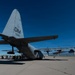 A large military transport aircraft, identifiable as a C-130 Hercules, is parked on a tarmac at what appears to be Davis-Monthan Air Force Base (indicated by the 'DM' tail code and serial number 590). The aircraft is photographed from a low rear angle, emphasizing the tail section and wings. A group of civilians and/or military personnel are gathered near the rear of the aircraft, suggesting a public event, tour, or static display.