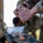 2026 US ARMY BEST SQUAD COMPETITION: Pistol Match A person wearing military camouflage (MultiCam/OCP pattern) is loading ammunition into a pistol magazine. A clear plastic bag containing loose brass-cased pistol cartridges is visible in the foreground on top of military gear. The image is a close-up shot with shallow depth of field, keeping the hands and ammunition in sharp focus.