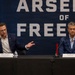 Two men are seated at a panel table in front of a large banner reading 'Arsenal of Freedom' with 'U.S. Department of War' branding visible in the background. Name placards identify the individuals as Bryan Chambers (Co-Founder &amp; President, Capital Factory) on the left and Pete Hegseth (Secretary of War, Department of War) on the right. The man on the left appears to be speaking while gesturing with his hand.