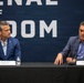 Two men are seated at a panel table with name placards identifying them as Pete Hegseth (Secretary of War, Department of War) and Emil Michael (Under Secretary of War for Research and Engineering, Department of War). They appear to be participating in a formal press conference or panel discussion in front of a large backdrop reading 'Arsenal of Freedom' with U.S. Department of War branding. The man on the right appears to be speaking while the man on the left listens.