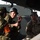 The image shows military personnel from at least two different armed forces engaged in what appears to be a briefing or discussion inside or alongside a military vehicle. One soldier wearing a black helmet and Japanese Ground Self-Defense Force (JGSDF) camouflage pattern uniform is speaking and gesturing, while a U.S. Army soldier in MultiCam/OCP uniform listens attentively. This appears to be a joint military exercise or training event between Japanese and American forces.