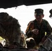 Three military personnel in camouflage uniforms are gathered around what appears to be a vehicle, reviewing documents or a map. The central figure is wearing an orange interpreter vest with Japanese characters (通訳/Interpreter) and a unit patch reading '11B', suggesting a joint US-Japanese military exercise. The soldier on the left has a visible name tape reading 'ALEXANDER' and 'US ARMY' patches.