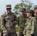 The image shows a group of military personnel from two different armed forces interacting in an outdoor setting. A U.S. Army soldier, identified by name tape 'MATBUYA' and U.S. Army insignia, is smiling and conversing with what appear to be Japan Ground Self-Defense Force (JGSDF) soldiers. The interaction appears friendly and relaxed, suggesting a joint training exercise or bilateral military engagement.