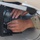 A military service member in MultiCam/OCP camouflage uniform is working on electronic equipment mounted inside what appears to be an aircraft or military vehicle panel. The person is using both hands to handle or install a black electronic component with heat sink fins and cable connections. The close-up shot focuses on the hands and the equipment being serviced.