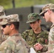 The image shows a group of military personnel from at least two different armed forces engaged in a discussion or briefing outdoors. U.S. Army soldiers wearing OCP (Operational Camouflage Pattern) uniforms are interacting with what appears to be a Japan Ground Self-Defense Force (JGSDF) soldier in a distinctive Japanese camouflage uniform. The setting suggests a joint military exercise or coordination meeting.