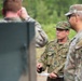 A Japan Ground Self-Defense Force (JGSDF) soldier, identified by his distinctive Japanese camouflage pattern and name tape reading 'KORU', appears to be briefing or instructing a group of U.S. Army soldiers wearing MultiCam/OCP uniforms. The setting appears to be an outdoor military training area with green vegetation in the background. This appears to be a joint military exercise or training event between Japanese and American forces.