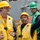 Delbert D. Black Conducts Replenishment-at-Sea with USNS John Lenthall Three workers are visible on what appears to be a naval vessel or industrial maritime setting. Two workers in yellow hard hats and yellow safety vests are in the foreground, with one gesturing and appearing to give directions or instructions. A third worker in a green hard hat and green vest stands in the background.
