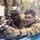 Yudh Abhyas 2026: U.S., Indian Soldiers exchange weapons, equipment knowledge in Auli Two military personnel in camouflage uniforms are positioned prone at what appears to be a shooting range or training facility. One soldier wearing a tactical helmet with face paint and a red-dot optic sight is aiming a rifle, while a second soldier wearing glasses appears to be providing instruction or guidance. Additional uniformed personnel are visible standing in the background.