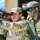 Yudh Abhyas 2026: U.S., Indian Soldiers exchange weapons, equipment knowledge in Auli The image depicts a joint military exercise involving soldiers from at least two nations, identifiable by an Indian flag patch and 'GARH RIF' (Garhwal Rifles) unit designation on one soldier's uniform. A soldier in MultiCam/OCP pattern camouflage is aiming a rifle equipped with an optical scope, while an Indian Army soldier in DPCU camouflage with tactical gear and face paint observes closely. A banner and Indian national flag are visible in the background, suggesting a formal bilateral training event.