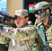 The image depicts a joint military exercise involving soldiers from at least two nations, identifiable by an Indian flag patch and 'GARH RIF' (Garhwal Rifles) unit designation on one soldier's uniform. A soldier in MultiCam/OCP pattern camouflage is aiming a rifle equipped with an optical scope, while an Indian Army soldier in DPCU camouflage with tactical gear and face paint observes closely. A banner and Indian national flag are visible in the background, suggesting a formal bilateral training event.