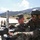 Yudh Abhyas 2026: U.S., Indian Soldiers exchange weapons, equipment knowledge in Auli Two soldiers, one wearing an Indian Army uniform with a tricolor flag patch and tactical helmet, and another in what appears to be US Army camouflage, are jointly examining or operating a mounted machine gun. The setting appears to be an outdoor military training area with mountainous terrain in the background. Additional soldiers in US Army uniforms are visible in the background, suggesting a joint military exercise or training event.