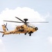 A military attack helicopter painted in desert tan/sand camouflage is captured in flight against a partly cloudy sky. The aircraft bears the word 'ARMY' on its fuselage along with what appears to be an Indian national roundel (tricolor cockade), identifying it as belonging to the Indian Army. The helicopter is equipped with weapons systems and sensor pods consistent with an AH-64 Apache attack helicopter configuration.