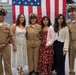 A group of six people pose for a photo in front of a large American flag in what appears to be a military facility or hangar. Three individuals are wearing U.S. Navy Chief Petty Officer dress khaki uniforms, while three others are in civilian attire. The occasion appears to be a military ceremony, likely a promotion or advancement event.