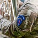 A close-up photograph of a U.S. Army soldier in MultiCam (OCP) camouflage uniform holding a brass instrument, likely a euphonium or baritone horn. A unit patch on the left sleeve reads 'USAREUR-AF BAND' with a blue shield design featuring a red torch/sword and rainbow arc, identifying the wearer as a member of the United States Army Europe and Africa Band. The image focuses on the uniform details and instrument rather than the soldier's face.