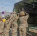 A group of U.S. Army soldiers in OCP (Operational Camouflage Pattern) uniforms and combat helmets are loading or unloading a litter/stretcher with a casualty into the rear of a military medical vehicle marked 'C22'. The scene appears to take place at a military installation in Germany, as evidenced by a German-language sign reading 'gesamter Bereich / entire area' alongside a no-parking road sign. This appears to be a medical evacuation (MEDEVAC) training exercise or actual casualty transport operation.