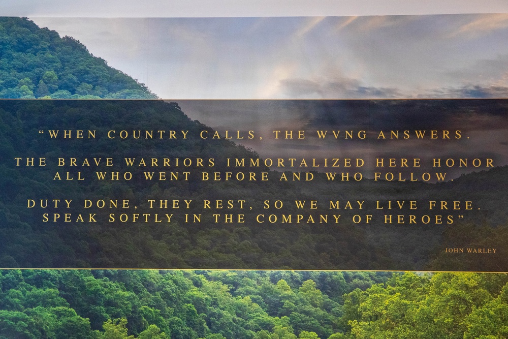The image displays an inspirational military quote by John Warley overlaid on a scenic landscape photograph featuring forested hills and a misty sky. The quote references the WVNG (West Virginia National Guard) and honors fallen warriors. It serves as a commemorative or memorial tribute graphic.