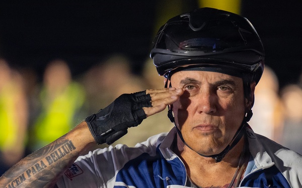 A middle-aged man wearing a cycling helmet and fingerless gloves is performing a military salute at what appears to be the 30th Annual Air Force Marathon. He is wearing a race bib numbered 79 labeled 'Sky Soldiers' for the Full Marathon category, along with a patriotic red, white, and blue cycling jersey. His forearm displays a tattoo reading 'Si Vis Pacem Para Bellum' (Latin for 'If you want peace, prepare for war').