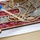 The image shows a craft project in progress, featuring a laser-cut wooden frame with an ornate tree or floral design being filled with small decorative gemstones or glass crystals in various colors. The stones include red, clear/gray, and amber/brown varieties arranged in sections defined by the wooden dividers. The piece appears to be resting on white parchment or wax paper during assembly.