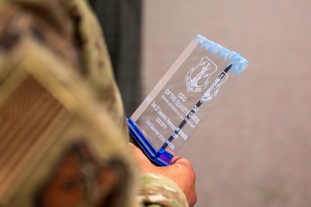A military service member in camouflage uniform holds a crystal glass award trophy. The award is engraved with 'CGO of the Quarter' for the Nevada Air National Guard, presented to 1st Lt Lauren Hernandez of the 152 CPTF for the 2nd Quarter 2026. The trophy features a blue base and jagged crystal top with an engraved unit emblem.