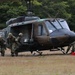 A military medical evacuation exercise is taking place on a grassy field. Soldiers wearing camouflage uniforms with Red Cross insignia are assisting a casualty near a Japanese Ground Self-Defense Force UH-1 Iroquois helicopter (tail number 41873). A second helicopter with a Japanese rising sun roundel is visible in the background.
