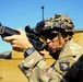 A U.S. Army soldier wearing MultiCam (OCP) camouflage and a tactical helmet is holding an M4-style carbine in a ready/aiming position. The soldier displays a 101st Airborne Division patch on the left shoulder. The image appears to be taken during a training exercise or operational deployment.