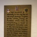 A bronze commemorative plaque mounted on a white wall, dedicated to the 82nd Airborne Division of the United States Army for their role in liberating Nijmegen during World War II. The plaque features three military/civic insignia at the top and raised lettering expressing gratitude to the division and the American people. It honors those who gave their lives during the liberation.