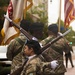 A military color guard unit is standing in formation during what appears to be a ceremonial parade or formal military event. The soldiers are wearing US Army OCP (Operational Camouflage Pattern) uniforms with black berets, white gloves, and are carrying ceremonial rifles and unit flags. At least one shoulder patch is visible showing what appears to be a ROTC or Army unit insignia.