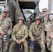 Four individuals pose in front of a vintage military truck, two wearing modern U.S. Army MultiCam (OCP) uniforms and two dressed in WWII-era U.S. Army photographer uniforms with steel helmets marked 'PHOTOGRAPHER'. All four are holding cameras, suggesting a photography-themed military commemoration or historical reenactment event. The name tape 'SILVERSMITH' is visible on the leftmost modern soldier.