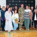 A group of approximately 15-20 people pose for a photo in front of an Army National Guard backdrop, celebrating what appears to be a military homecoming or deployment ceremony. One person in the center is wearing a U.S. Army camouflage uniform, surrounded by smiling family members and friends. A sign reading 'Brave Enough to Serve. Loved Enough to be Missed. Strong Enough to Come Home.' is prominently displayed.